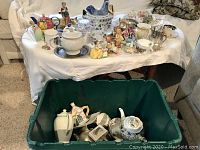 Photo of assorted mixed china, glassware, and collectibles arranged on a table and in a green bin