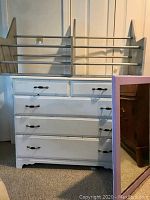 Photo showing the solid wood bureau with five drawers, new black handles, large wooden shoe rack placed on top, and the matching mirror leaning beside it.