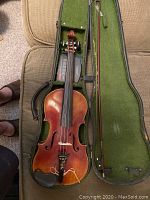 Full view of the violin inside the open hard case showing the violin body, bow and the green felt case lining.