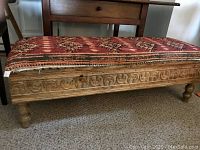 Front side view of the carved wooden bench showing carved detail and upcycled fabric padded top.