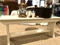 Ivory-colored painted bench with simple design and lower shelf, placed on carpeted floor.