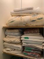 Linen closet shelf showing multiple folded sheets, blankets, and labeled sheet sets.