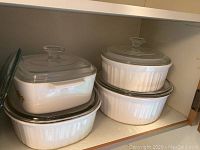 Three white CorningWare casserole dishes with glass lids, one rectangular with sunflower pattern, two round dishes.