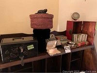 Full view of the lot items on a wooden shelf, showing the black lacquer jewelry box, woven basket, and various small boxes including the red wooden box with ink stamps