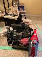 Full overview of all electronics laid out on carpet, showing phones, case with missing reel recorder, vacuum, discs, and accessories.