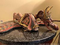 Close-up photo of the carved wood dragon sculpture displaying colorful wings and gold accents, placed on a black table surface.