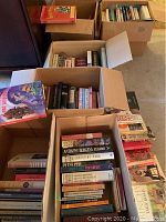 Boxes filled with assorted fiction and nonfiction books, hardcover and softcover, stacked and packed closely.