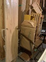 Photo showing stacked wooden shelving boards in light wood finish, wrapped in packaging along with some wire racks and a cardboard bag labeled 'shelf'