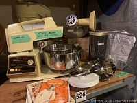 Full view of Oster stand mixer with metal mixing bowls and various attachments displayed on a table with manuals.