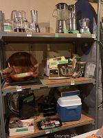Front view of metal shelving unit loaded with wooden trays, coolers, kitchen appliances, and various household items (not included in lot).