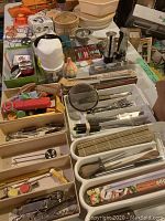 Overview photo showing a wide assortment of kitchen items including dishes, knives, corkscrews, peelers, and trays laid out on table.