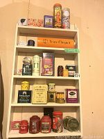 Photo of a white shelf with vintage and decorative tins including tea tins, branded tins, and a Veuve Clicquot box
