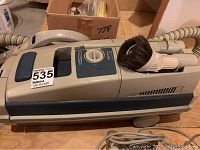 Side view of gray and blue vintage Electrolux vacuum and floor polisher with attached hose and brush head.