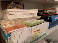 Stack of various office paper supplies including note pads, memo pads, and envelopes stacked on a shelf.