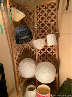Variety of lamp shades hanging on room divider including blue velour shade, white fabric, and paper lantern style shades