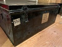 Photo of black metal travel trunk side showing clasps and original label sticker