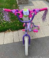 Front view of the pink and purple girls bicycle with training wheels and handlebar streamers.