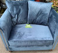 Close-up front view of blue velvet tub chair with two matching throw pillows inside the seat area.