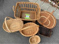 Set of six assorted wicker baskets arranged on pavement, showing various shapes, sizes, and a basket with wheels.