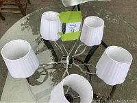 Top-down view of the silver tone 5 light chandelier showing the unique shaped center bar and five white fabric shades with pleats.