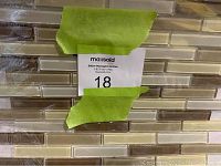 Photo showing close-up of glass mosaic tile sheets with rectangular glossy tiles in beige and brown tones, with auction lot label visible.