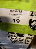 Photo showing the box label with auction and lot information, partially revealing the pattern of one tile underneath green tape.