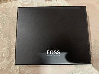 Closed black Hugo Boss box with logo on lid shown on a beige patterned surface.