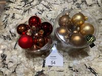Two clear plastic containers on marble surface holding 20 glass Christmas ornaments total, one container with gold-toned ornaments and the other with red and copper tones