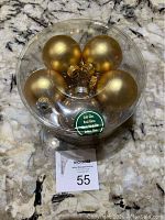 Photo of 5 gold glass Christmas ornaments arranged in a clear plastic container, showing shine and metallic caps