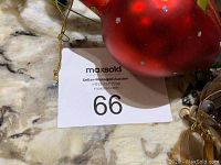 Photo showing closeup of lot number 66 and part of a large red round glass ornament.