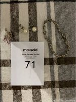 Photo showing a silver-tone linked chain bracelet and three pairs of earrings on a striped fabric background.