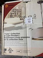 Box showing product branding, name, and specifications including chrome trimmed fabric shade, glass diffuser, satin nickel finish, and adjustable length.