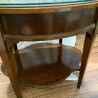 Close-up view of the curved legs, wood frame with brass or gold trim beneath the glass top, and lower wood shelf.