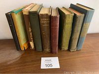 Photo of nine antique hardcover books on wood surface, showing colors, sizes, and wear