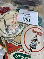 Plastic bag containing multiple vintage drinking coasters featuring different brand logos and designs, including Budweiser and saxophone-themed coasters.