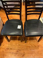 Top view of two black leather dining chairs showing seat surfaces and wear marks.