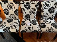 Three upholstered dining chairs with white fabric featuring large black floral designs, showing wear and stains.