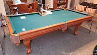 Brunswick oak framed pool table with claw feet and green felt surface, setup indoors on carpet.