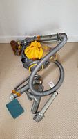 Photo showing the Dyson vacuum main unit with attached long flexible hose and several attached accessories on carpeted floor.