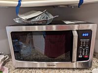 Front view of Toshiba microwave with digital display at 0:00 and control panel visible.