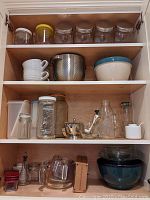 Shelves with glass jars, ceramic bowls, metal colander, and glass bottles, sugar bowl