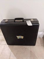 Black carrying case for metal detector with WE logo and handle with two clasps.