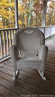 Front view of white wicker rocking chair on porch, showing woven design and overall shape