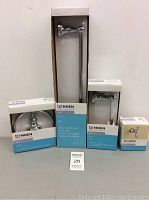 Lot contents include four boxed Moen chrome bathroom accessories on a table against a plain wall.