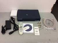 Full view of AverMedia DVR box, remote, power adapter, installation CD, BNC connectors, and Ethernet cable on table.