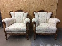 Front view of both chairs showing floral upholstery, rolled arms, carved wood frame, and brass rivet embellishments.