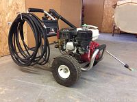 Angled front-left view of pressure washer showing engine, frame and coiled hose