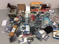 Wide shot of assorted computer parts and accessories including power supply unit, cables, adapters, and small components laid on a gray surface.