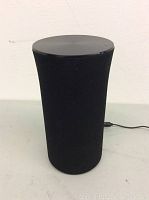 Front and side view of the black cylindrical wireless speaker showing fabric body and rounded top.