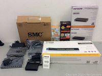 Wide shot of multiple boxed and unboxed network switches including Netgear ProSAFE, SMC, and Tenda, with accessories like power adapters and cables.